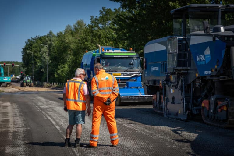 Twee medewerkers lopen langs het materieel op de weg